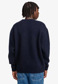 Marinblå stickad tröja med rund halsringning, sänkta axlar och ribbade muddar och nederkant. Lätt och mjuk kvalitet med en avslappnad passform.