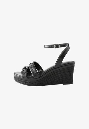 Sandales compensées noires avec une plateforme en jute tressé, présentant des lanières texturées croisées et une sangle de cheville réglable. Talon plat.