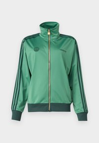 Grön sportig zip-up jacka med hög krage, guld dragkedja, tre mörkgröna ränder på ärmarna och logotyp på bröstet.