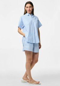 Zila un baltā svītraina īsās piedurknes krekla un saskaņotu šortu komplekts, kas piedāvā pogājamu priekšpusi, brīvu piegriezumu un sānu kabatas.