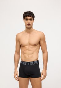 Czarne bawełniane bokserki z szerokim elastycznym pasem, na którym znajduje się szare logo "CALVIN KLEIN". Gładka tekstura, dopasowany krój.