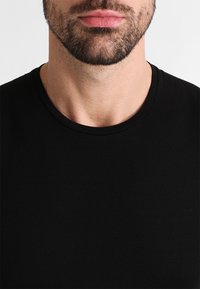 Svart crew-neck t-skjorte laget av glatt, lett stoff, med korte ermer og en tettsittende passform rundt halsen og skuldrene.