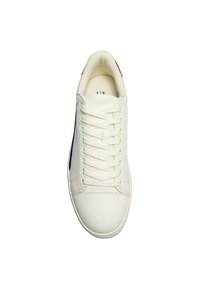 Weiße Sneaker mit einem strukturierten Canvas-Obermaterial, flachen Schnürsenkeln und einer Gummisohle. Verfügt über einen dunkelblauen seitlichen Streifen und einen roten Akzent an der Ferse.