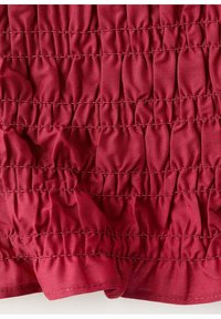 Gros plan d’un tissu rouge profond avec des rangées horizontales de coutures élastiques froncées créant une texture plissée et un bord froncé en bas.