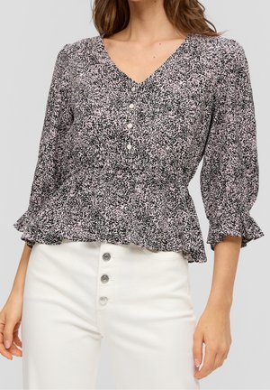 Schwarze und rosa gemusterte Bluse mit V-Ausschnitt, Knopfverschluss und gerafften Ärmeln. Kombiniert mit weißen, hoch taillierten Hosen mit dekorativen Knöpfen.