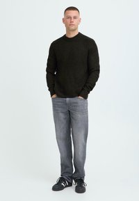 Mørkegrønn ribbestrikket genser, grå straight-leg jeans og sorte joggesko med hvite striper. Minimalistisk design, teksturert stoff, uformell passform.