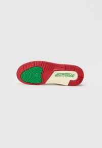 Czerwono-zielona gumowa podeszwa trampka z okrągłymi i teksturowanymi wzorami. Wytłoczone logo "JORDAN" w zielonym kolorze na kremowym tle.