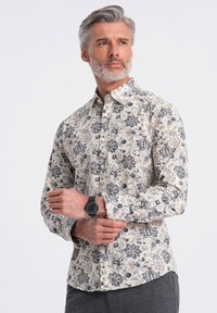 Langærmet skjorte med knapper i creme med blå og orange blomsterprint. Letvægtsstof med klassisk krave. Har knapmanchetter.