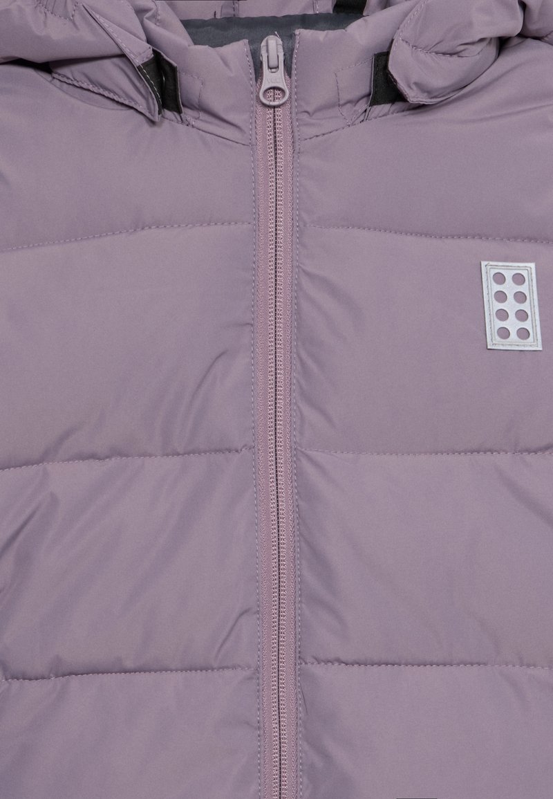 Puffjacke in Helllila, mit einem zentralen Reißverschluss und Zuglasche, horizontal gestepptem Muster und einem kleinen Logo-Patch mit Punkten.