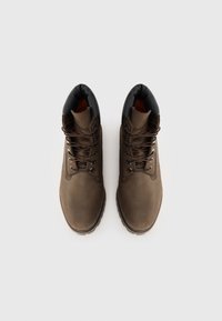 Bottes chelsea en cuir marron avec une surface lisse, un col rembourré noir, des lacets marron et une semelle robuste pour une bonne adhérence.