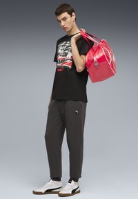 Sort grafisk t-shirt, grå sweatpants og hvide sportssko. Holder en skinnende pink håndtaske med lynlås og to hanke.
