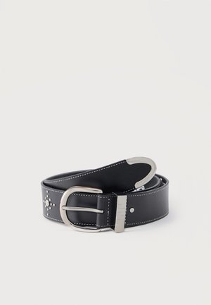 Zwarte lederen riem met zilveren gesp, decoratieve metalen studs in een kruispatroon en witte stiksels langs de randen, opgerold op een witte achtergrond.