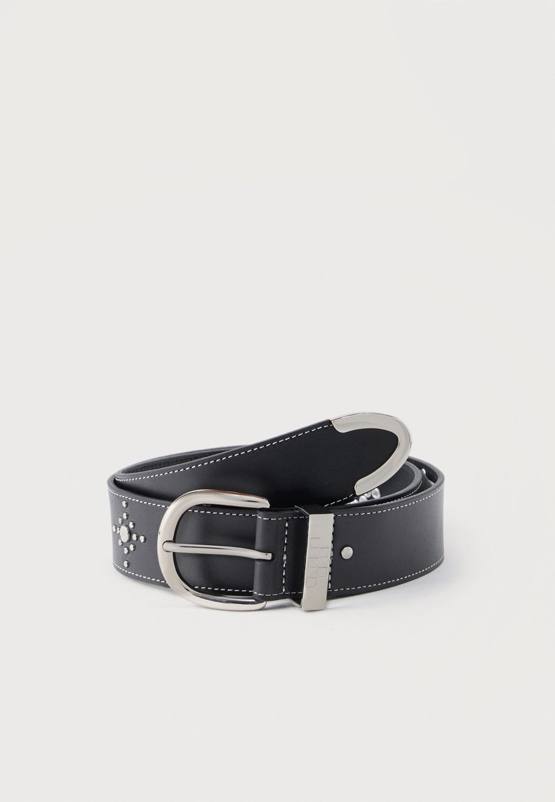 Černý kožený pásek se stříbrnou sponou, dekorativními kovovými nýty ve tvaru kříže a bílým prošitím okolo okrajů, stočený na bílém pozadí.