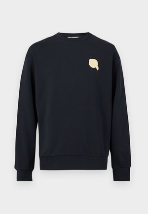 Juodas ilgomis rankovėmis megztinis su apvalia apykakle, ant kairiojo krūtinės šono yra mažas smėlio spalvos rankos logotipas, o rankogaliai bei apačia yra ribuotos.