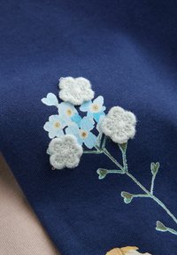 Tela azul marino con flores bordadas en azul claro y blanco suave con tallos verdes; detalles intrincados en los patrones florales.