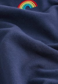 Tessuto blu navy con una superficie morbida, caratterizzato da un dettaglio arcobaleno ricamato in colori vivaci nell'angolo in alto a sinistra.