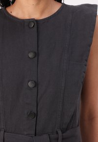 Vestido sem mangas de cor cinza escuro com decote redondo, apresentando botões na parte frontal, costuras verticais e uma cintura amarrada.