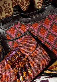 Due borse: una grande in pelle nera con un motivo intrecciato arancione e rosa, e una borsa più piccola decorata con ornamenti colorati di perline.