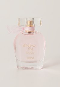 Przezroczysta szklana butelka perfum o okrągłym kształcie, z jasnoróżowym płynem, złotym napisem oraz różową wstążką na szyjce. Korek jest przezroczysty.