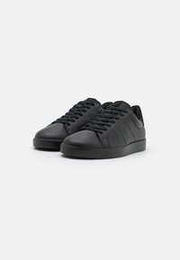 Sneaker in pelle nera con punte tonde, lacci piatti e una finitura liscia. Design minimalista con dettagli di cucitura sottili e un tallone testurizzato.
