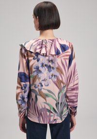 Blouse à manches longues en tissu doux, avec un col froncé, dans des teintes de rose et de violet, et un imprimé botanique détaillé sur l'ensemble.