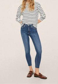 Jeans ajustados azules con cintura alta, combinados con una camiseta de rayas blancas y navy de mangas largas. Mocasines marrones completan el atuendo.