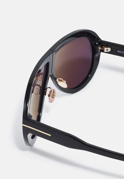 Occhiali da sole neri con lenti sfumate, hardware dorato e un design del telaio elegante. I dettagli notevoli includono forme angolari e accenti minimali.