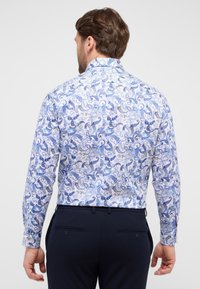Witte shirt met blauwe paisleypatroon, lange mouwen en een button-down kraag. Draag met donkere broek, laat de achterkant en de stofstructuur zien.