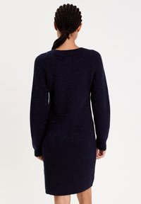 Dzianinowa sukienka w ciemnogranatowym kolorze z prążkowaną fakturą, długimi rękawami i dopasowanym krojem, z delikatnymi metalicznymi akcentami w całej powierzchni.