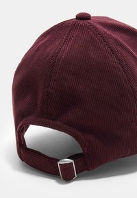 Bordová kordurová baseballová čiapka s zaoblenou korunou, textúrovaným materiálom a nastaviteľným remienkom so strieborným hardvérom vzadu.