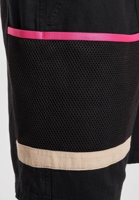 Schwarze Shorts mit einer Netztasche, leuchtend pinkem Akzentband und einem beigen Stoffband im unteren Bereich. Strukturierten Details sind sichtbar.