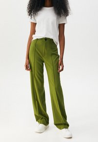 Grüne, maßgeschneiderte, hochtaillierte Hose mit geradem Schnitt, vorderen Falten, einem einzelnen Knopf und einer glatten Textur.