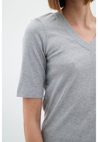 Szary, prążkowany t-shirt z dekoltem w serek i krótkimi rękawami, wykonany z miękkiego materiału o teksturowanym wzorze. Zbliżenie na górną część ciała.