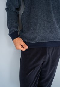 Chemise à manches longues bleu marine avec un motif rayé texturé et des poignets sombres, associée à un pantalon en tissu doux et foncé. Coupe décontractée, texture lisse.