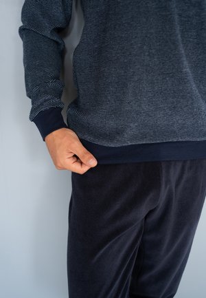 Chemise à manches longues bleu marine avec un motif rayé texturé et des poignets sombres, associée à un pantalon en tissu doux et foncé. Coupe décontractée, texture lisse.