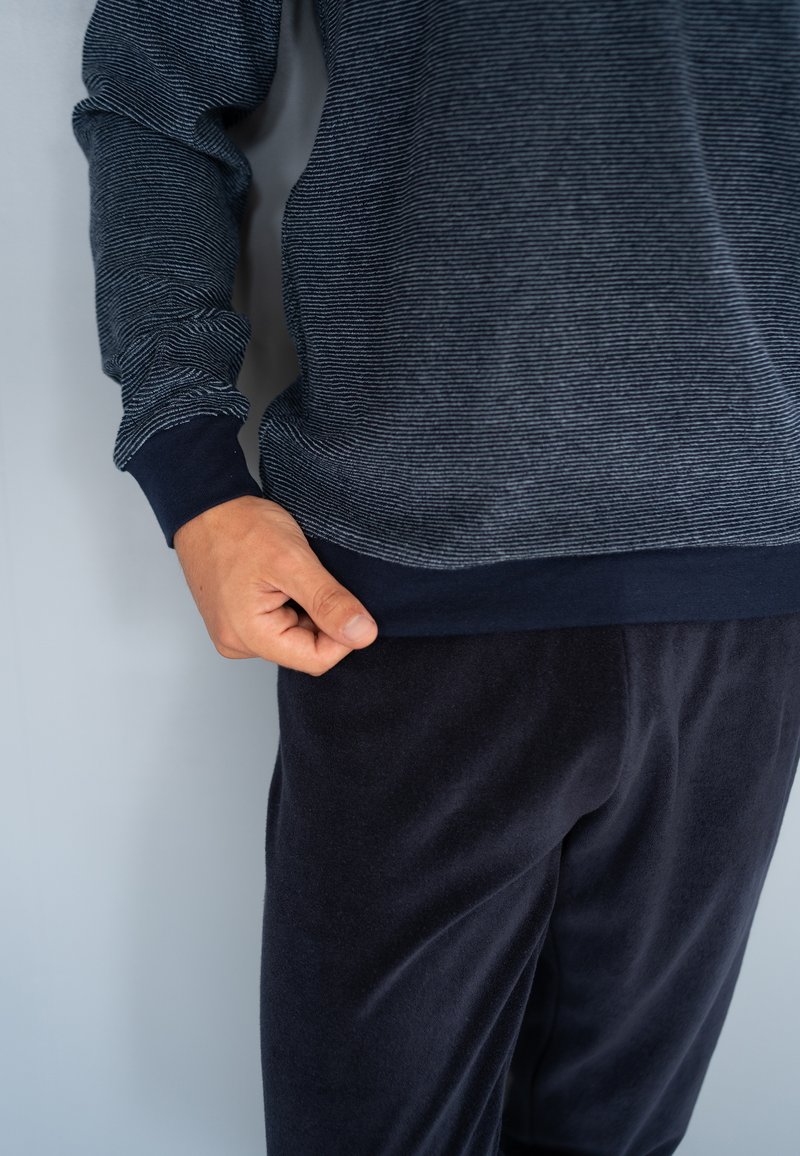 Chemise à manches longues bleu marine avec un motif rayé texturé et des poignets sombres, associée à un pantalon en tissu doux et foncé. Coupe décontractée, texture lisse.