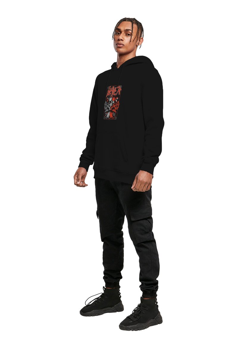 Sort hættetrøje med grafisk print, der har kranier og røde detaljer. Foran er der en kængurulomme og hætte med snoretræk. Sammen med sorte joggers og støvler.