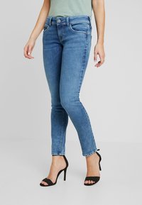 Jeans skinny blu in denim, con vita media, cinque tasche e design casual, abbinati a sandali neri open-toe.