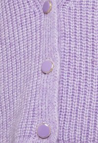 Lila stickad kofta med ett texturerat mönster, med fyra runda, ljuslila knappar och guldaccenter längs knappslån.