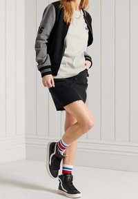 Minifalda de mezclilla negra con dobladillo deshilachado, chaqueta bomber gris y negra, camiseta gris, zapatillas negras y calcetines a rayas en rojo, blanco y azul.