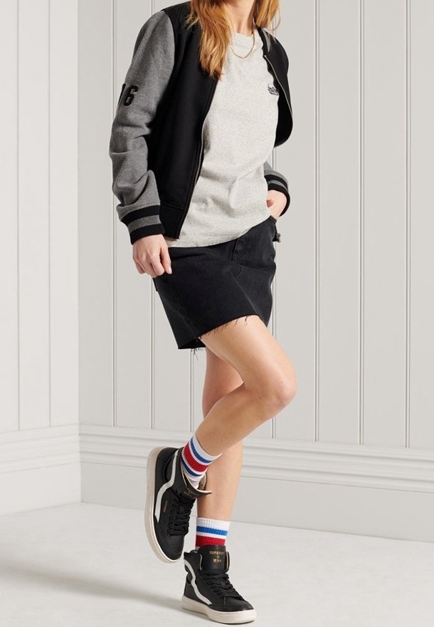Minifalda de mezclilla negra con dobladillo deshilachado, chaqueta bomber gris y negra, camiseta gris, zapatillas negras y calcetines a rayas en rojo, blanco y azul.
