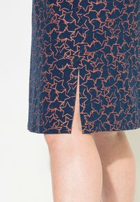 Marinblå kjol med stjärnmönster i korall, med en sidoklyvning. Tillverkad av texturerad tyg, har den en figursydd design.