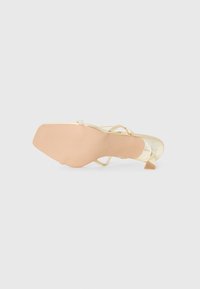 Nude stiletto sandal med firkantet hæl, metallisk gull aksenter og tynne, krysset remmer med dekorativ rhinestone detaljer.