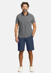 Pantalones cortos azul marino combinados con una camisa polo a cuadros que presenta un cuello y puños en contraste. Llevado con zapatillas blancas.