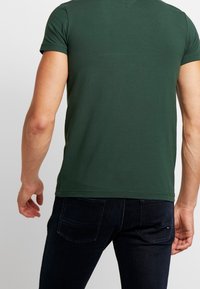Grøn kortærmet t-shirt lavet af blød bomuld, med rund hals og tæt pasform, parret med mørke denim jeans med baglommer.