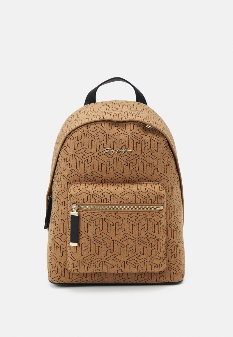 Sac à dos marron avec motif abstrait "TH" noir, poche avant zippée, poignée noire et petit logo doré au centre en haut.