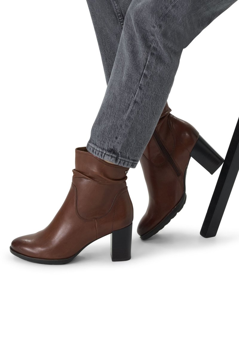 Bottines en cuir marron au design élégant, avec un bout arrondi, un talon bloc haut et un tige douce et froncée. Semelle noire visible.