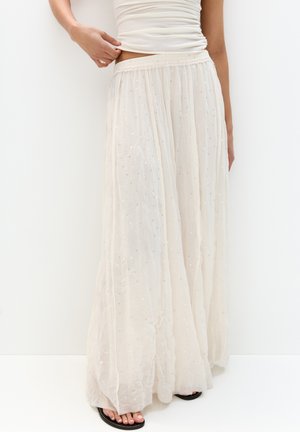 Jupe maxi longue, fluide et crème en tissu léger avec des accents brodés et des sequins. Ceinture élastique pour plus de confort.