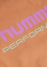 Orange stof med en glat tekstur, der har stort lilla "hummel" tekst og mindre aqua "PERFORMANCE" tekst.