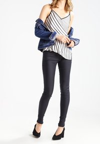 Pantalones ajustados negros combinados con una blusa sin mangas a rayas y una chaqueta de mezclilla. La blusa tiene un escote en V y un diseño asimétrico. Unos tacones negros completan el look.